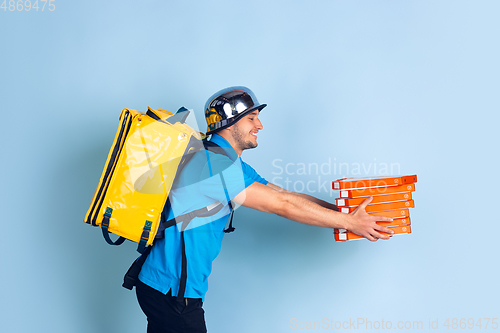 Image of Contacless delivery service during quarantine. Man delivers food and shopping bags during insulation. Emotions of deliveryman isolated on blue background.