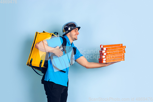 Image of Contacless delivery service during quarantine. Man delivers food and shopping bags during insulation. Emotions of deliveryman isolated on blue background.