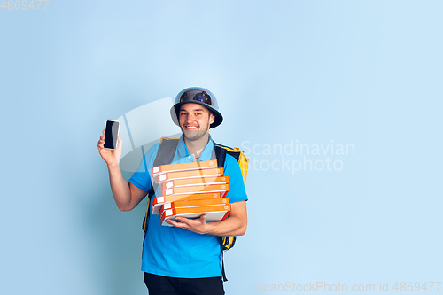 Image of Contacless delivery service during quarantine. Man delivers food and shopping bags during insulation. Emotions of deliveryman isolated on blue background.