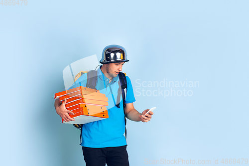 Image of Contacless delivery service during quarantine. Man delivers food and shopping bags during insulation. Emotions of deliveryman isolated on blue background.