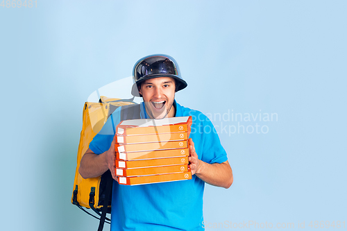 Image of Contacless delivery service during quarantine. Man delivers food and shopping bags during insulation. Emotions of deliveryman isolated on blue background.