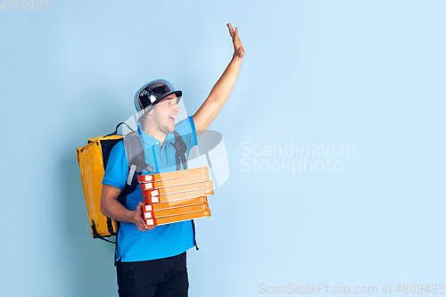 Image of Contacless delivery service during quarantine. Man delivers food and shopping bags during insulation. Emotions of deliveryman isolated on blue background.