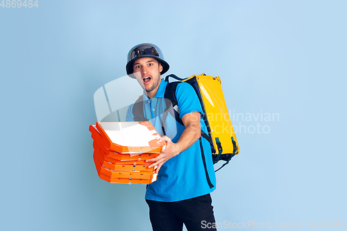 Image of Contacless delivery service during quarantine. Man delivers food and shopping bags during insulation. Emotions of deliveryman isolated on blue background.