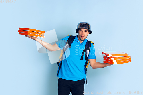 Image of Contacless delivery service during quarantine. Man delivers food and shopping bags during insulation. Emotions of deliveryman isolated on blue background.