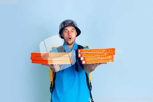 Image of Contacless delivery service during quarantine. Man delivers food and shopping bags during insulation. Emotions of deliveryman isolated on blue background.