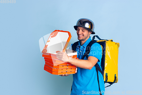 Image of Contacless delivery service during quarantine. Man delivers food and shopping bags during insulation. Emotions of deliveryman isolated on blue background.