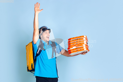 Image of Contacless delivery service during quarantine. Man delivers food and shopping bags during insulation. Emotions of deliveryman isolated on blue background.