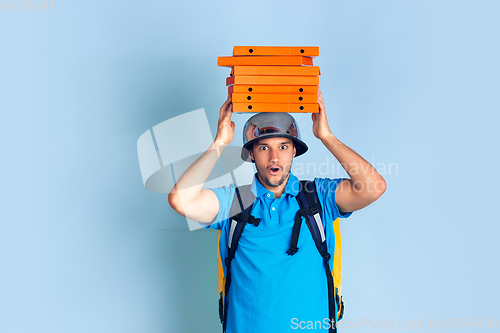 Image of Contacless delivery service during quarantine. Man delivers food and shopping bags during insulation. Emotions of deliveryman isolated on blue background.