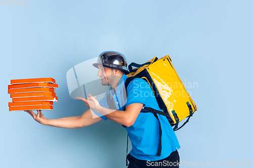 Image of Contacless delivery service during quarantine. Man delivers food and shopping bags during insulation. Emotions of deliveryman isolated on blue background.