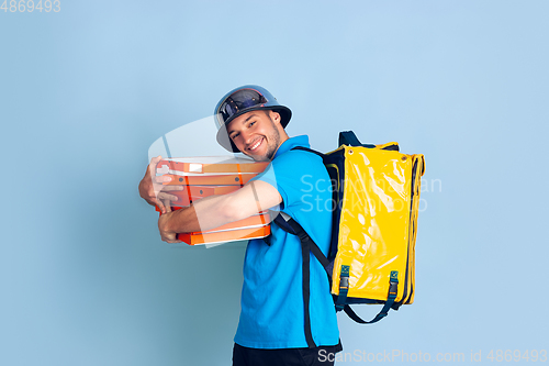 Image of Contacless delivery service during quarantine. Man delivers food and shopping bags during insulation. Emotions of deliveryman isolated on blue background.