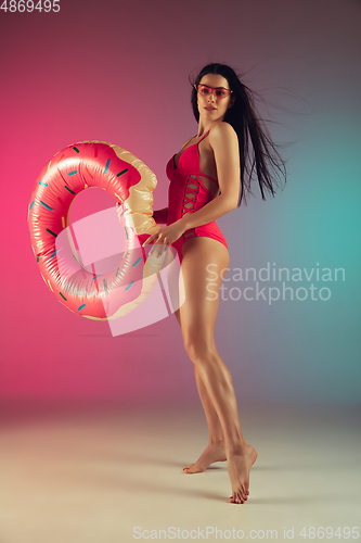 Image of Fashion portrait of young fit and sportive woman in stylish pink luxury swimwear with rubber donut on gradient background. Perfect body ready for summertime.