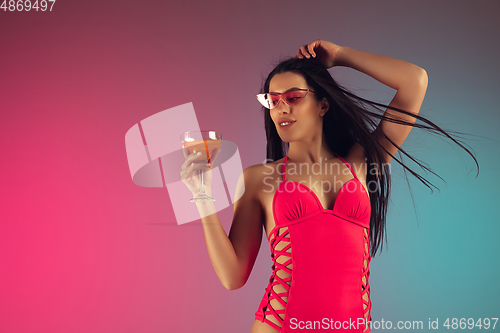 Image of Fashion portrait of young fit and sportive woman in stylish pink luxury swimwear with cocktail on gradient background. Perfect body ready for summertime.