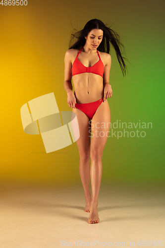 Image of Fashion portrait of young fit and sportive woman in stylish red luxury swimwear on gradient green-yellow background. Perfect body ready for summertime.
