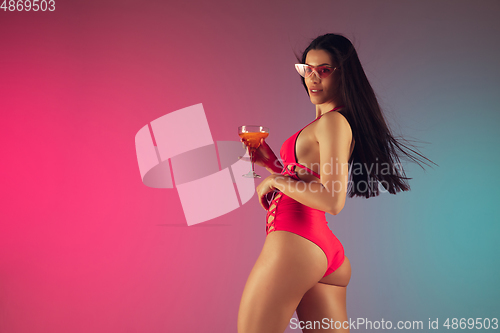 Image of Fashion portrait of young fit and sportive woman in stylish pink luxury swimwear with cocktail on gradient background. Perfect body ready for summertime.