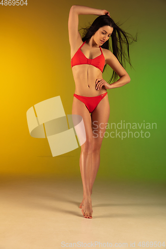 Image of Fashion portrait of young fit and sportive woman in stylish red luxury swimwear on gradient green-yellow background. Perfect body ready for summertime.