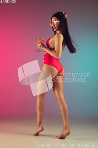 Image of Fashion portrait of young fit and sportive woman in stylish pink luxury swimwear with cocktail on gradient background. Perfect body ready for summertime.