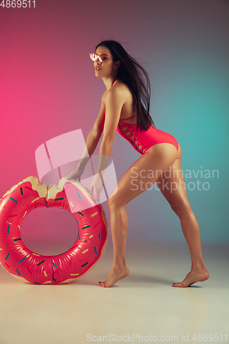 Image of Fashion portrait of young fit and sportive woman in stylish pink luxury swimwear with rubber donut on gradient background. Perfect body ready for summertime.