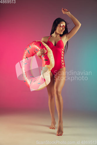 Image of Fashion portrait of young fit and sportive woman in stylish pink luxury swimwear with rubber donut on gradient background. Perfect body ready for summertime.