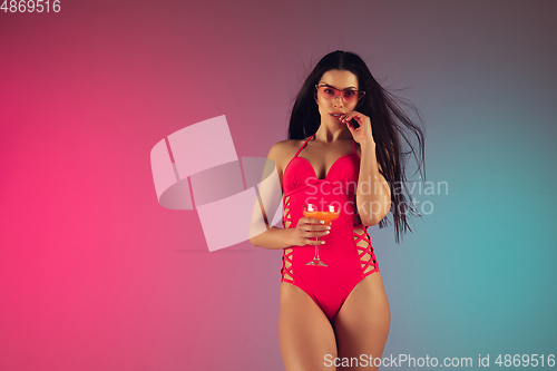 Image of Fashion portrait of young fit and sportive woman in stylish pink luxury swimwear with cocktail on gradient background. Perfect body ready for summertime.