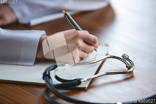 Image of Close up of doctors hands with stethoscope, sheets and pills on wooden background