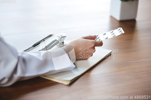Image of Close up of doctors hands with stethoscope, sheets, giving pills to patient on wooden background