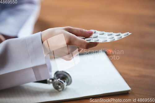 Image of Close up of doctors hands with stethoscope, sheets, giving pills to patient on wooden background