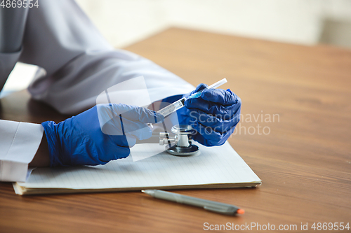 Image of Close up of doctors hands wearing blue protective gloves with stethoscope and syringe on wooden table background