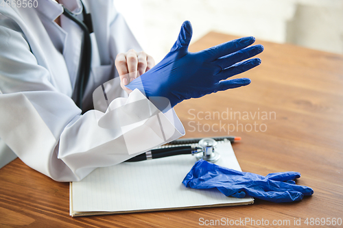 Image of Close up of doctors hands wearing blue protective gloves on wooden table background