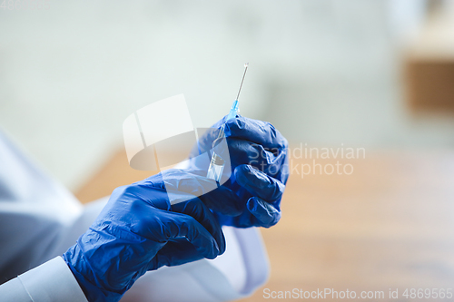 Image of Close up of doctors hands wearing blue protective gloves with syringe on wooden table background