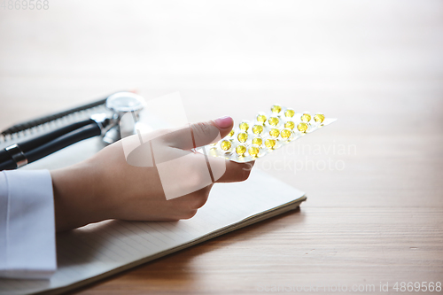 Image of Close up of doctors hands with stethoscope, sheets, giving pills to patient on wooden background