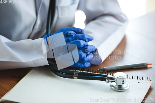 Image of Close up of doctors hands wearing blue protective gloves with stethoscope on wooden table background