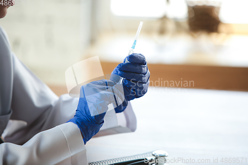 Image of Close up of doctors hands wearing blue protective gloves with stethoscope and syringe on wooden table background