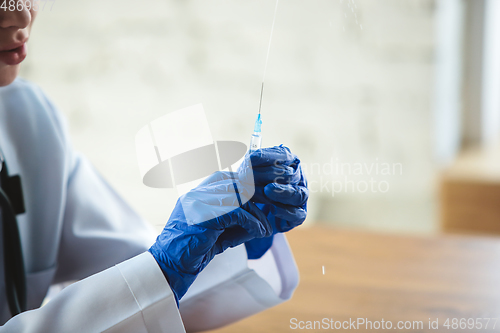 Image of Close up of doctors hands wearing blue protective gloves with syringe on wooden table background