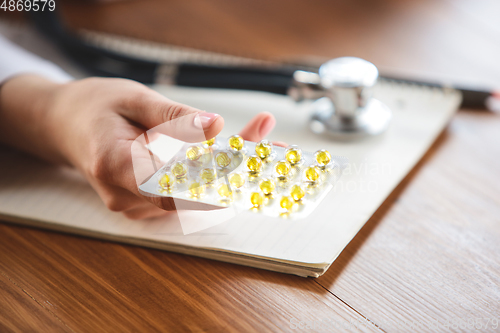 Image of Close up of doctors hands with stethoscope, sheets, giving pills to patient on wooden background