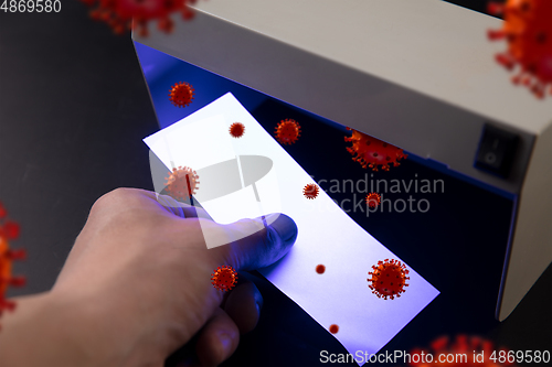 Image of Male hands checking of banknotes in the detector, 3D models of coronavirus spreding around