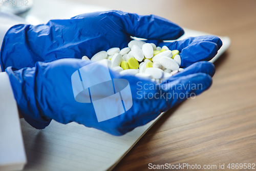 Image of Close up of doctors hands wearing blue protective gloves giving bunch of pills on wooden table background