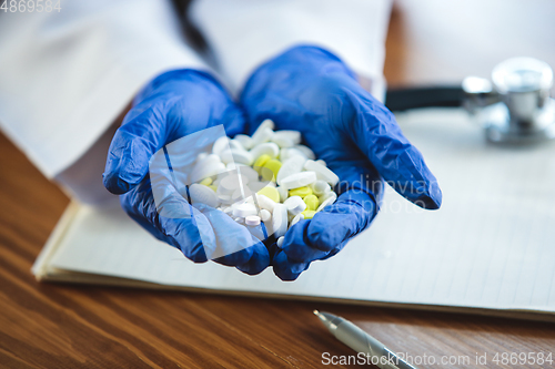 Image of Close up of doctors hands wearing blue protective gloves giving bunch of pills on wooden table background