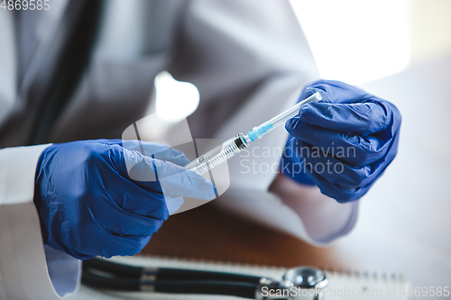 Image of Close up of doctors hands wearing blue protective gloves with stethoscope and syringe on wooden table background