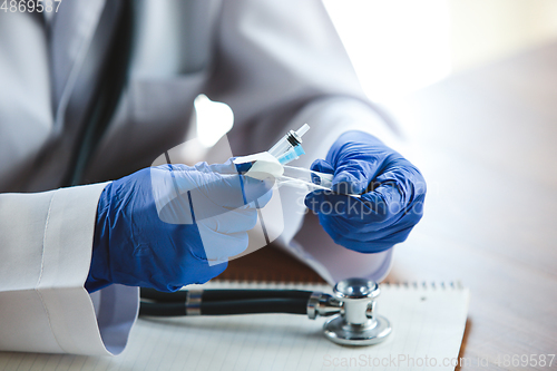 Image of Close up of doctors hands wearing blue protective gloves with stethoscope and syringe on wooden table background