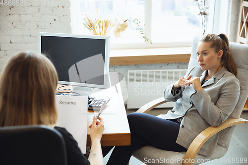 Image of Young woman in suit sitting in office during the job interview with female employee, boss or HR-manager, talking, thinking, looks confident