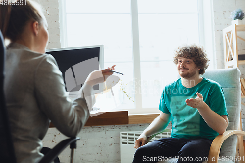 Image of Young man sitting in office during the job interview with female employee, boss or HR-manager, talking, thinking, looks confident