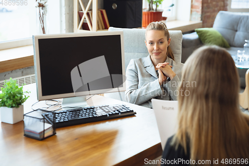 Image of Young woman in suit sitting in office during the job interview with female employee, boss or HR-manager, talking, thinking, looks confident