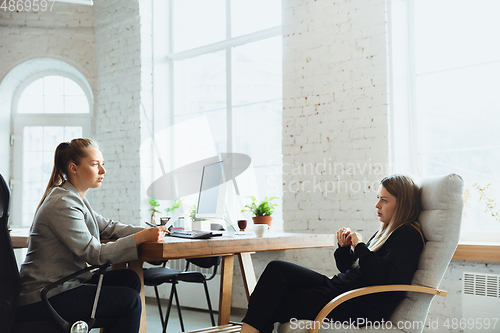 Image of Young woman sitting in office during the job interview with female employee, boss or HR-manager, talking, thinking, looks confident