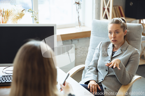 Image of Young woman in suit sitting in office during the job interview with female employee, boss or HR-manager, talking, thinking, looks confident