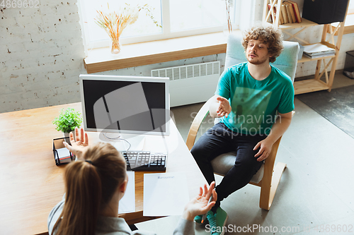 Image of Young man sitting in office during the job interview with female employee, boss or HR-manager, talking, thinking, looks confident