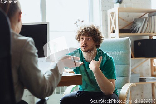 Image of Young man sitting in office during the job interview with female employee, boss or HR-manager, talking, thinking, looks confident