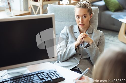 Image of Young woman in suit sitting in office during the job interview with female employee, boss or HR-manager, talking, thinking, looks confident