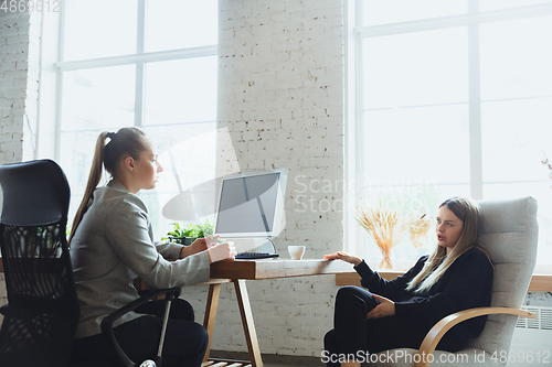 Image of Young woman sitting in office during the job interview with female employee, boss or HR-manager, talking, thinking, looks confident