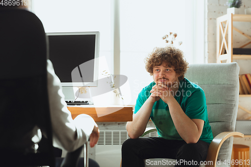 Image of Young man sitting in office during the job interview with female employee, boss or HR-manager, talking, thinking, looks confident