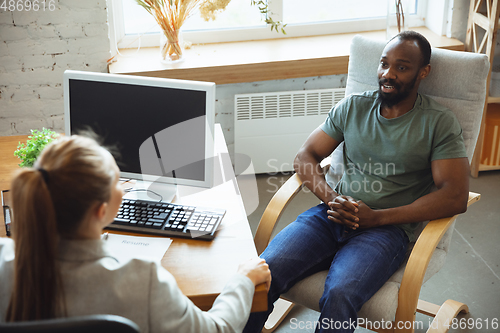 Image of Young man sitting in office during the job interview with female employee, boss or HR-manager, talking, thinking, looks confident